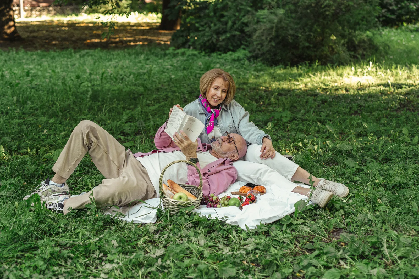 A couple relaxing with a book and a picnic on the grass in a park